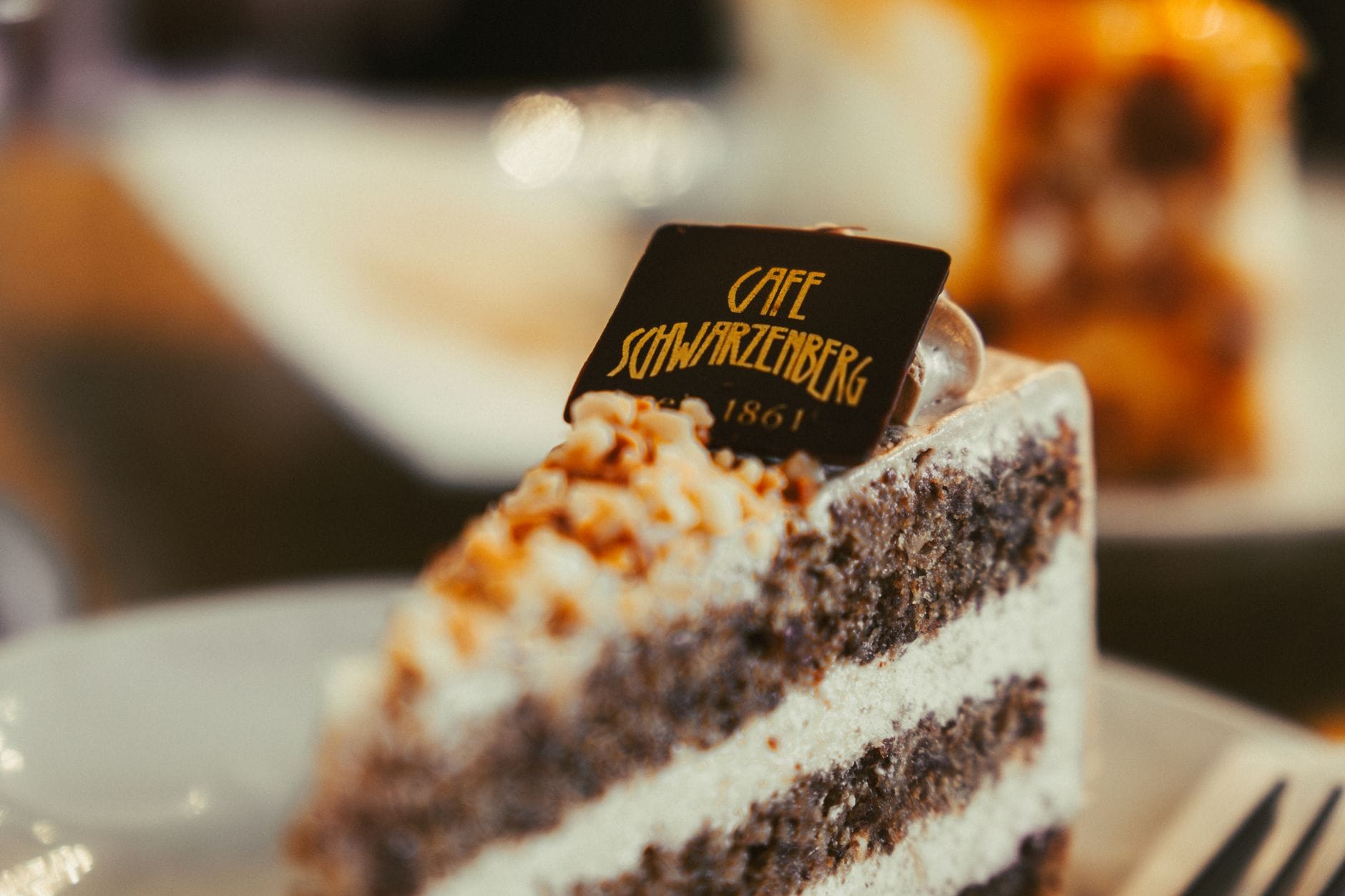 Nahaufnahme eines Stücks geschichteter Schokoladentorte mit Schlagobers und Nüssen auf einem weißen Teller in einem Wiener Kaffeehaus.