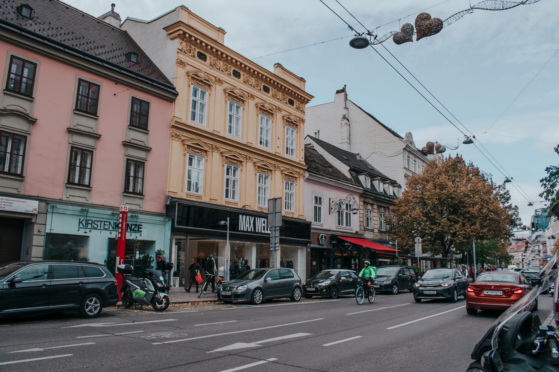 Straßenansicht im Wiener Neubau-Viertel mit kleinen unabhängigen Geschäften, Fußgängern und Radfahrern entlang eines lebhaften städtischen Gehwegs.