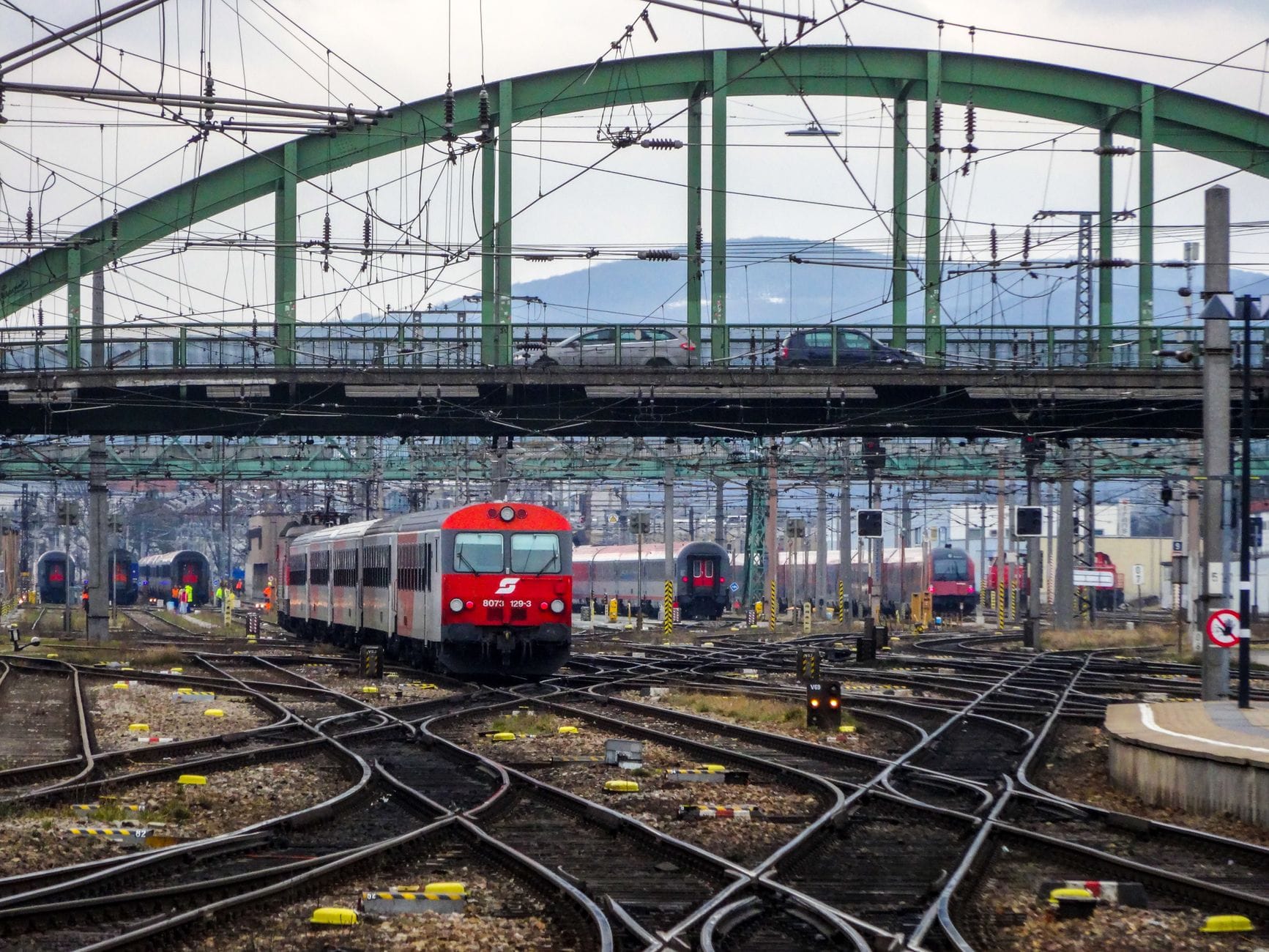 Un concurrido depósito ferroviario en Viena con varios trenes de ÖBB, vías convergentes y una estructura de puente de hierro verde elevada.