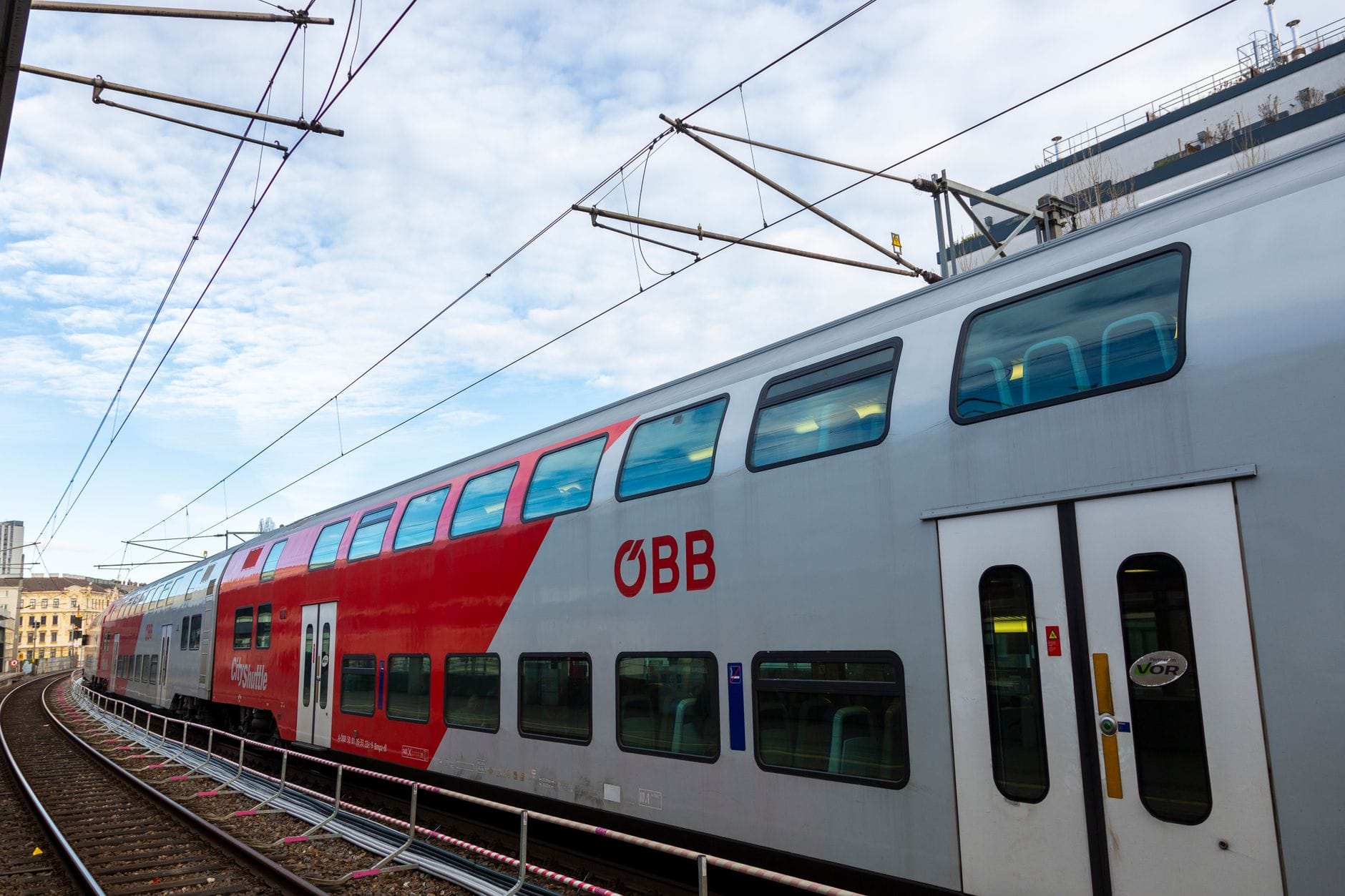 Ein moderner ÖBB-Doppelstockzug an einem Bahnhof mit geschwungenen Gleisen und blauem Himmel – ein Sinnbild für Bahnreisen in Österreich zwischen Städten wie Wien und Salzburg.