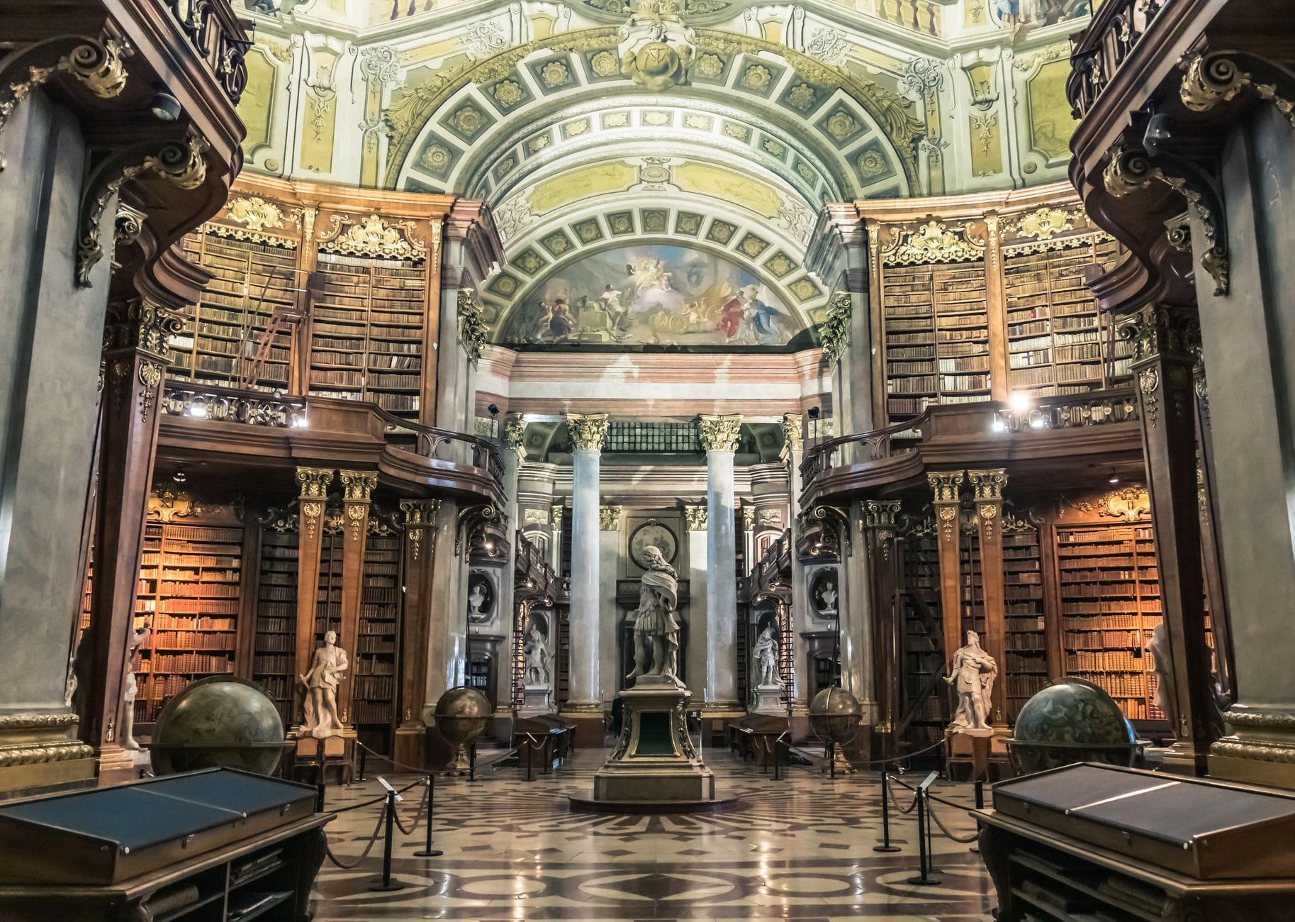 Vista grandangolare della magnifica sala barocca della Biblioteca Nazionale Austriaca a Vienna, con colonne ornate, affreschi sul soffitto e una statua
