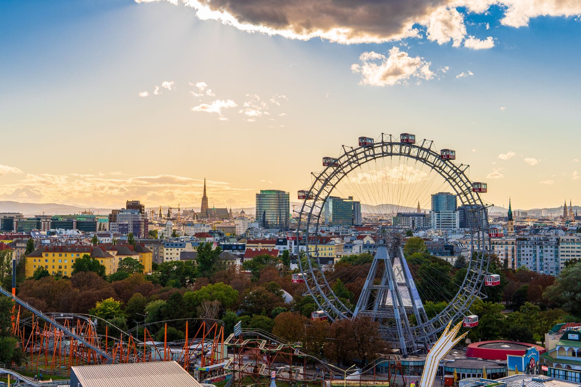 Weitblick über Wien mit dem berühmten Riesenrad im Prater, Fahrgeschäften und der Stadtsilhouette unter einem dramatischen Himmel.