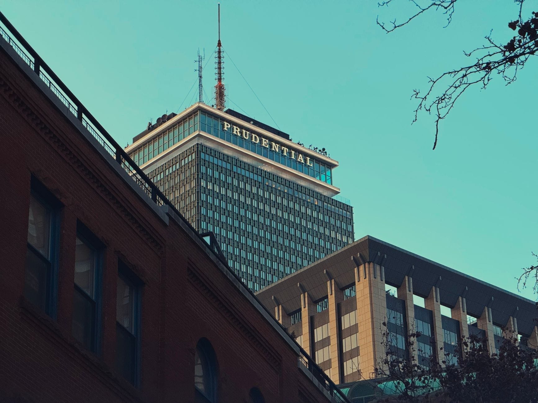 La Prudential Tower si erge sopra gli edifici circostanti a Boston, con i suoi piani superiori visibili sotto un cielo azzurro limpido.