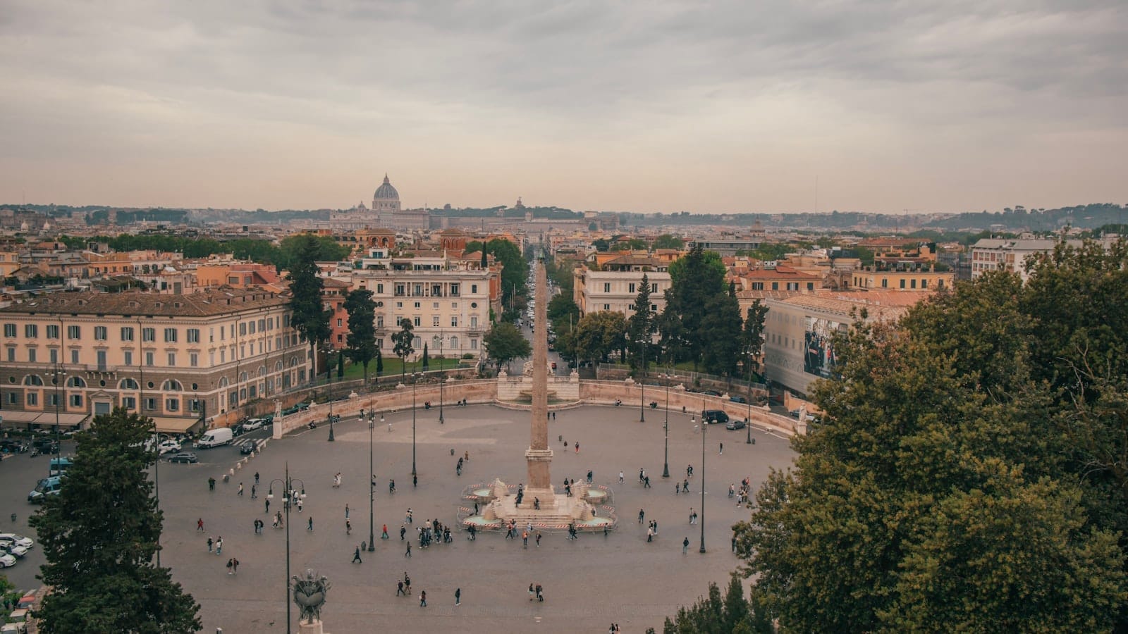Panoramic view of Piazza del Popolo and the city skyline as seen from the Pincio terrace in Rome, with trees and buildings under a softly overcast sky.