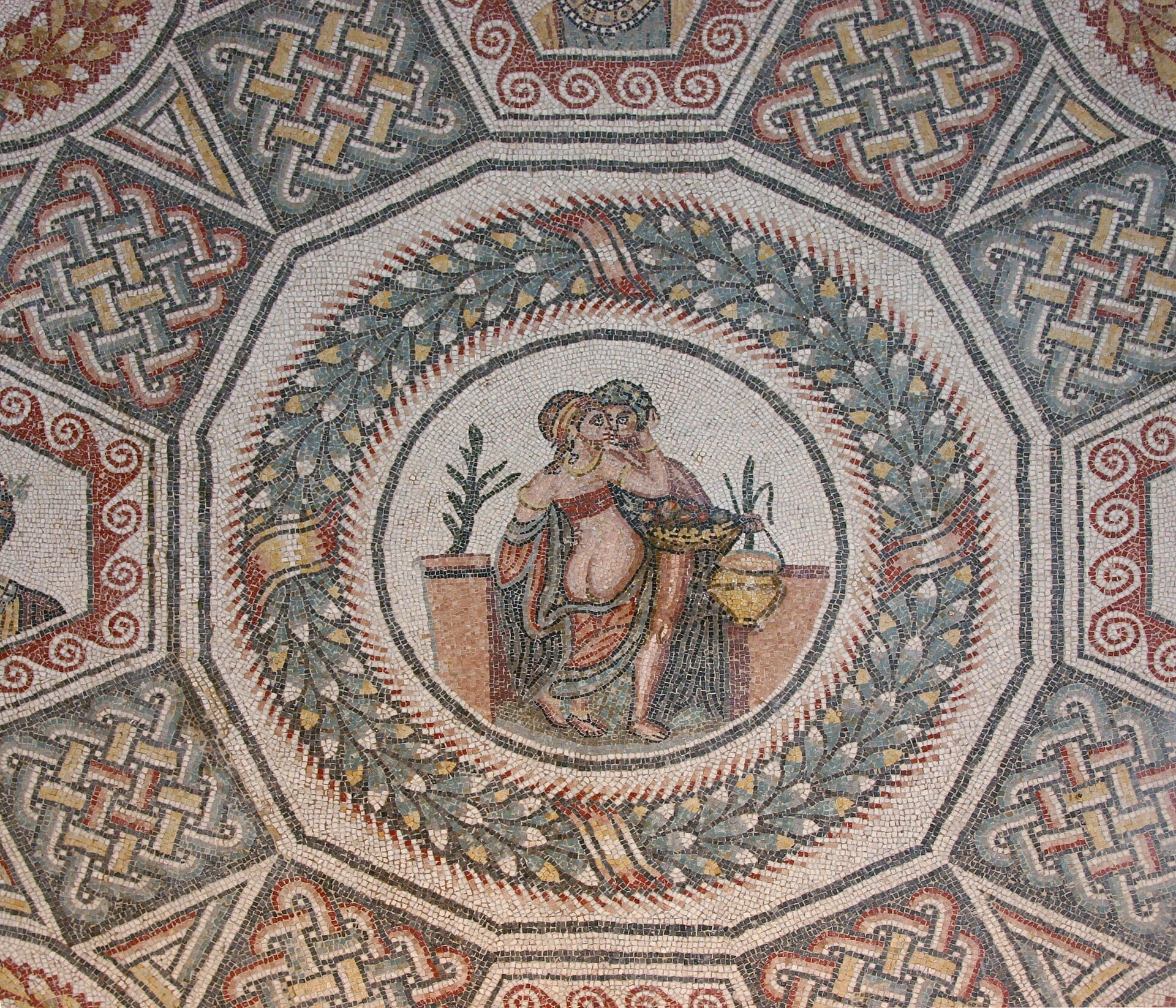 Detaillierter römischer Mosaikboden in der Villa Romana del Casale mit lebhaften geometrischen Mustern und einer zentralen Szene zweier Figuren, umgeben von Lorbeerkränzen.