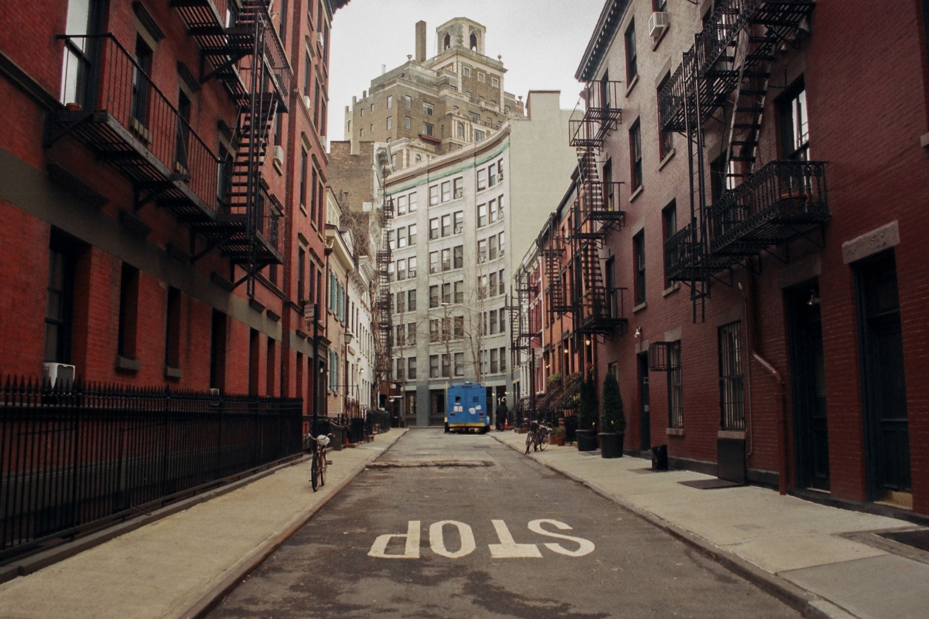 Vista lungo una strada stretta e classica di New York nel Greenwich Village, con edifici in mattoni rossi e scale antincendio che evocano l'atmosfera senza tempo della città.