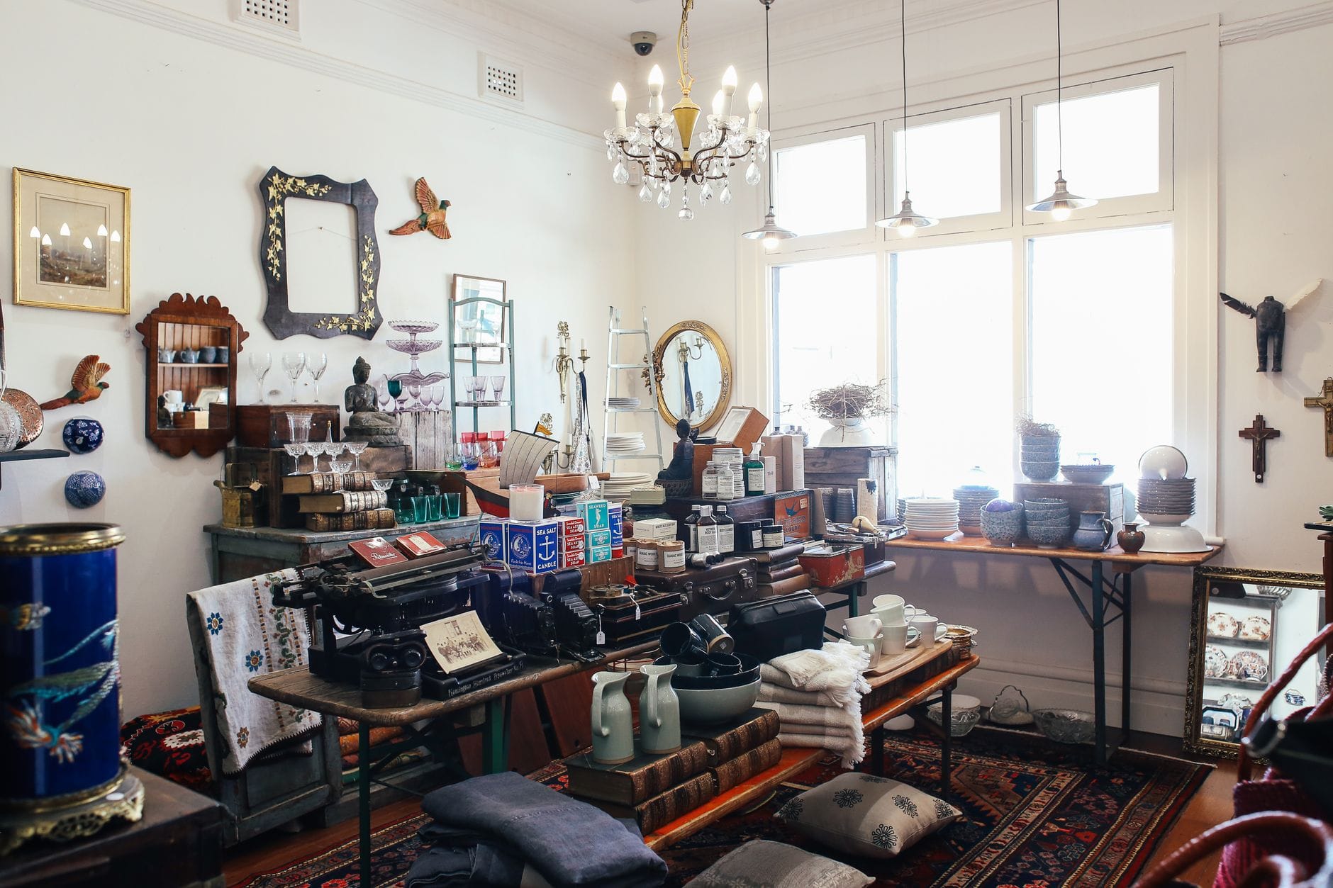 Intérieur lumineux et accueillant d'une boutique d'antiquités avec décoration vintage, céramiques, miroirs, machine à écrire et objets de collection disposés sur des tables et des étagères.