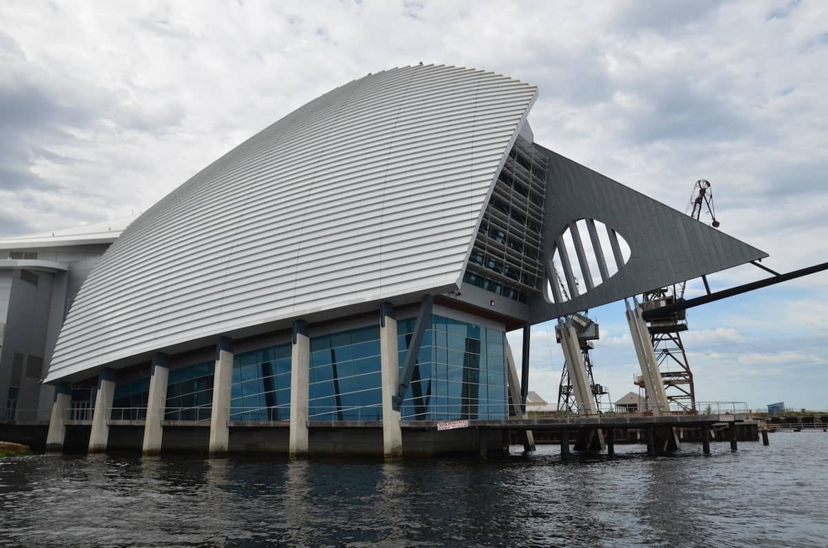 Das moderne, weiße und verglaste Gebäude des WA Maritime Museum thront über dem Wasser am Victoria Quay mit Kränen und bewölktem Himmel im Hintergrund.
