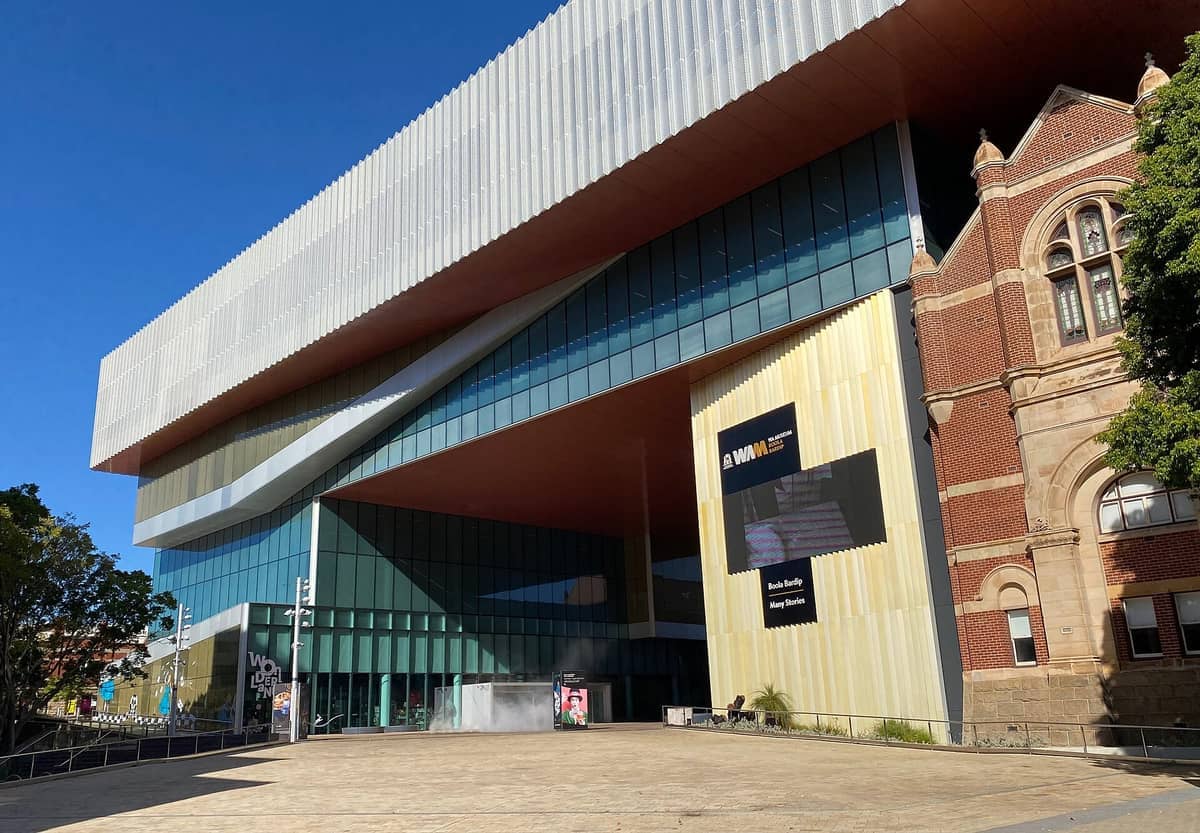 Außenansicht des WA Museum Boola Bardip mit moderner Glas- und Metallarchitektur neben restaurierten roten Backsteingebäuden unter einem klaren blauen Himmel.