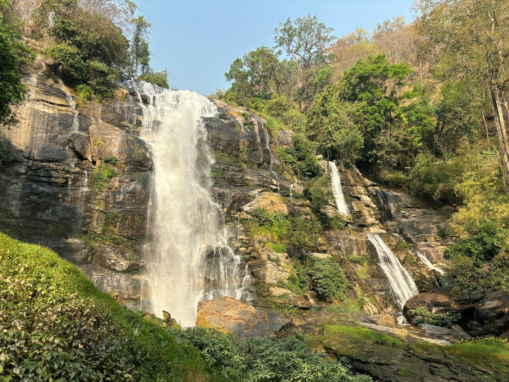 La cascada Wachirathan cayendo por un acantilado rocoso rodeado de exuberante bosque verde, bajo un cielo despejado en el Parque Nacional Doi Inthanon.
