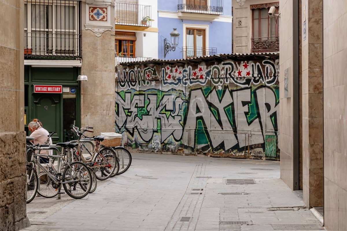 Calle estrecha en Valencia con bicicletas y mural de grafiti, típica del ambiente animado y urbano de El Carmen.