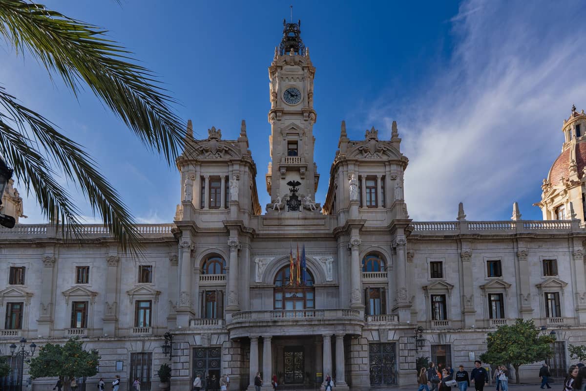 Vista amplia del edificio del Ayuntamiento de Valencia con palmera y personas paseando en la plaza cívica principal en un día soleado