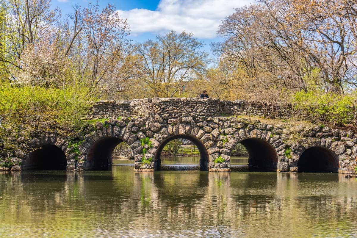 Puente de piedra con múltiples arcos que cruza un estanque sereno en un exuberante paisaje de parque durante la primavera.