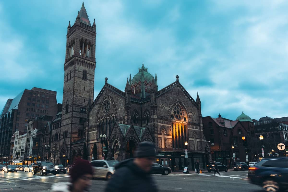 Trinity Church en Back Bay de Boston, iluminada al anochecer con edificios de la ciudad cercanos y una calle concurrida en primer plano.