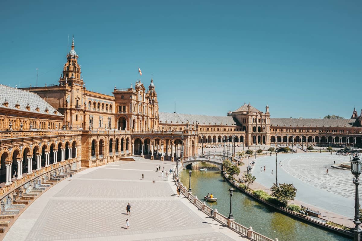 มุมกว้างของ Plaza de España เซบีย่า โชว์อาคารรูปร่างโค้ง หอคอย คลอง และลานกว้างภายใต้ท้องฟ้าสีฟ้าสดใส