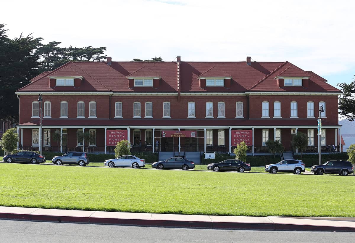 Vista frontal del Walt Disney Family Museum con su fachada de ladrillo rojo y tejado rojo, visto desde el césped del Presidio.