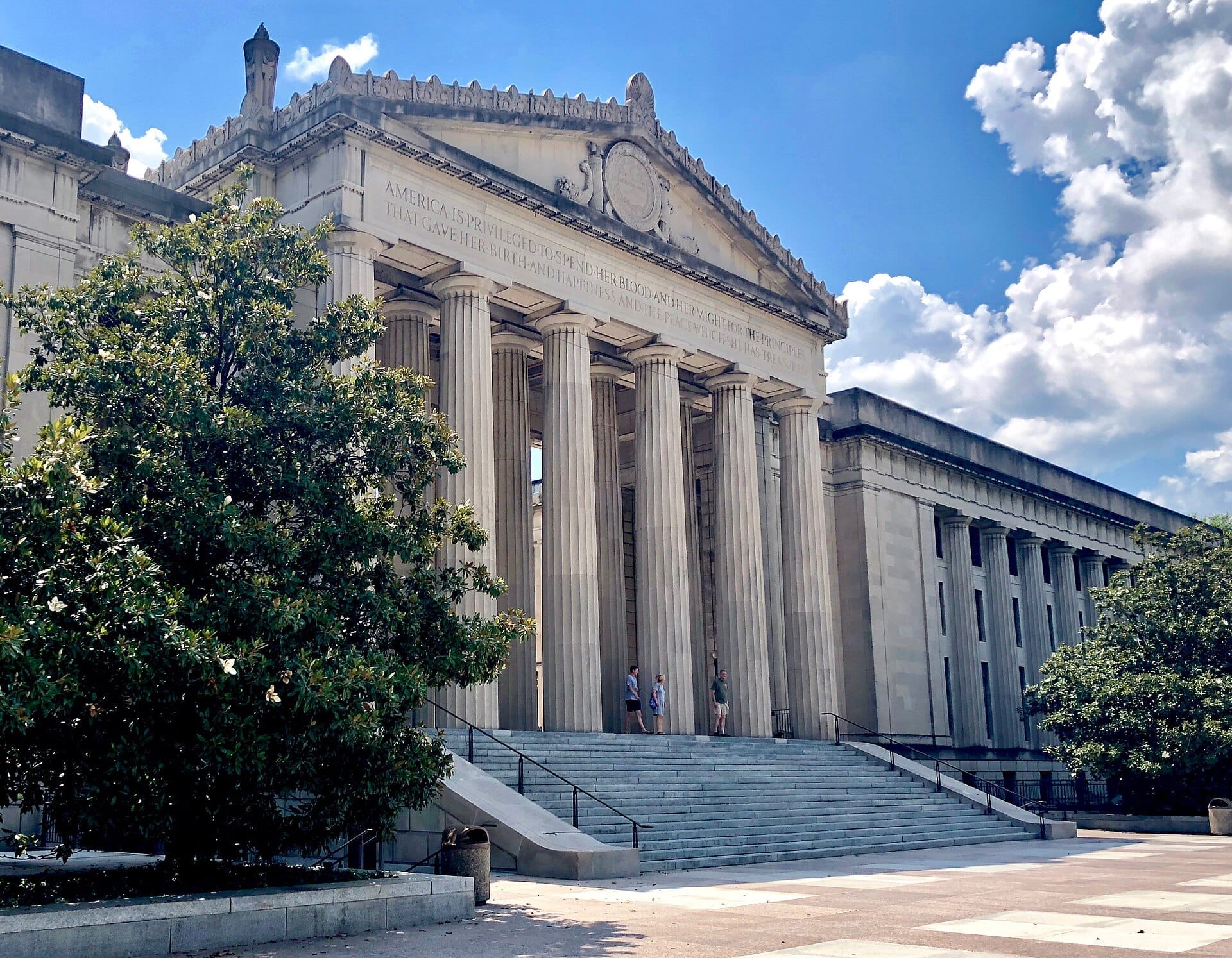 Fachada grandiosa de estilo Beaux-Arts del War Memorial Auditorium con altas columnas y escalones, enmarcada por árboles verdes bajo un cielo azul brillante de Nashville.