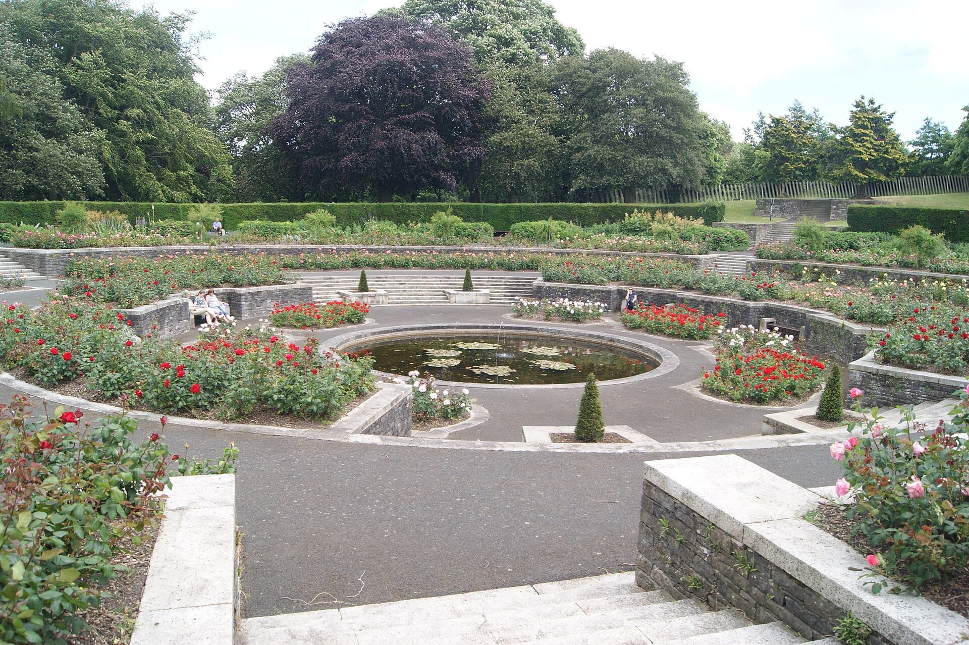 Stagno circolare con ninfee circondato da camminamenti in pietra a gradoni e giardini di rose in fiore agli Irish National War Memorial Gardens, Dublino.