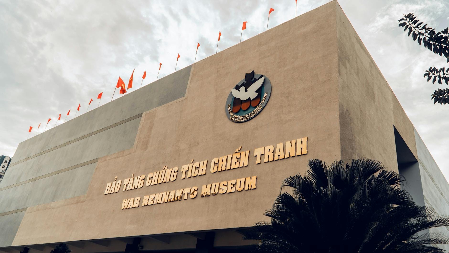 La fachada del Museo de los Vestigios de la Guerra con su nombre en vietnamita e inglés, fotografiada desde abajo bajo un cielo dramático.