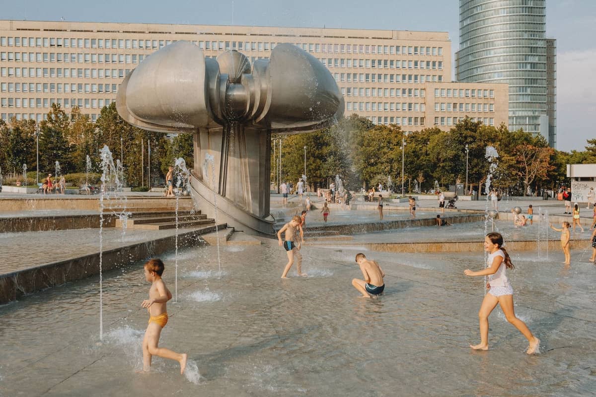 Kinder spielen und rennen durch moderne Brunnen auf einem Stadtplatz in Warschau mit einer einzigartigen Skulptur und Stadtgebäuden im Hintergrund.