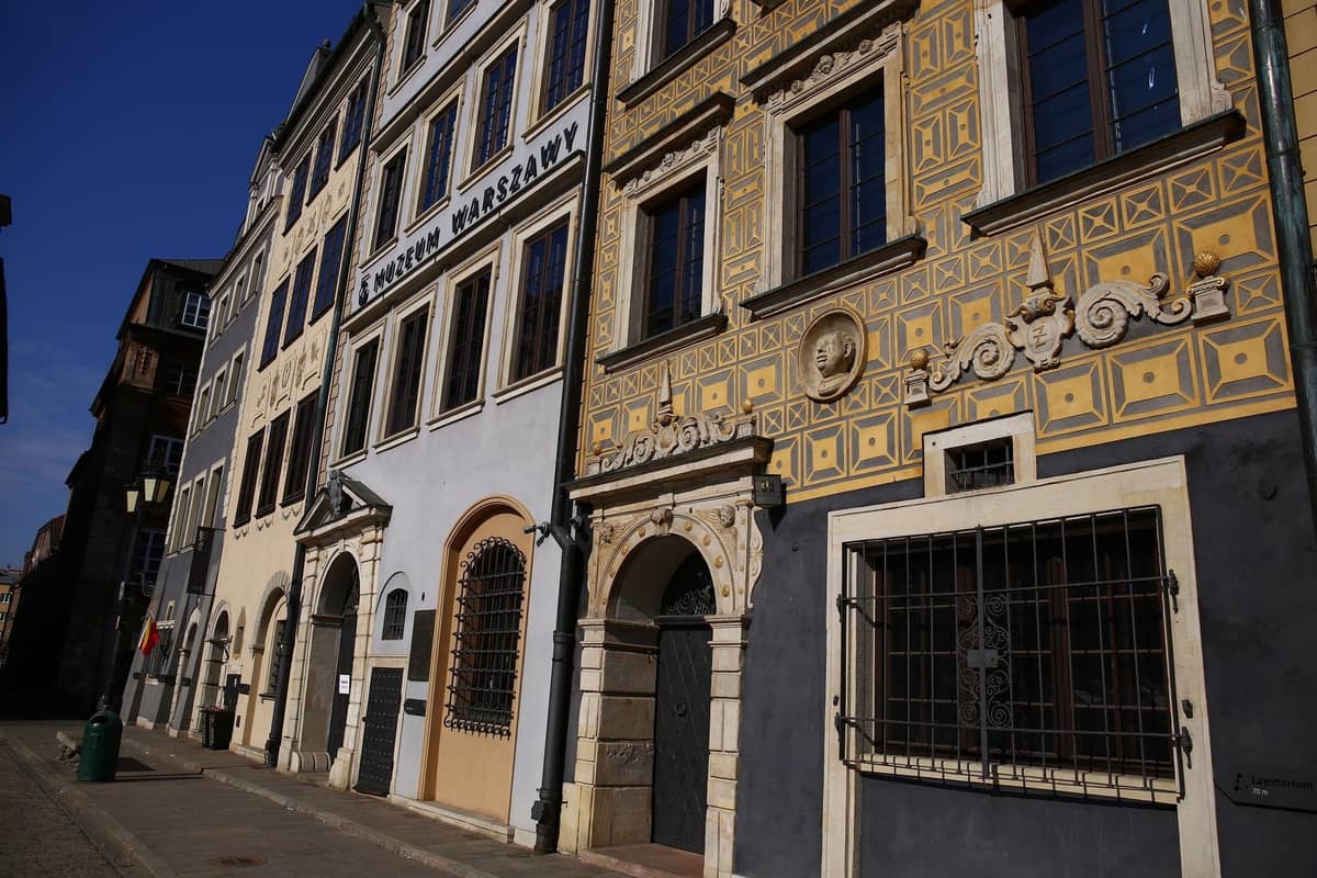 Rząd zabytkowych budynków z szyldem Muzeum Warszawy, przedstawiający wejście do Muzeum Warszawy w jasnym świetle dnia.