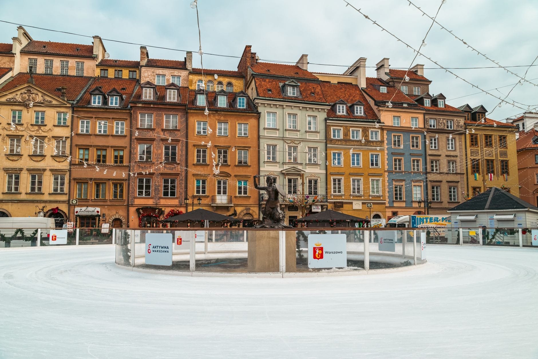 Os coloridos prédios da Cidade Velha de Varsóvia ao fundo de uma pista de patinação no gelo rodeada de neve, capturando a animada atmosfera de inverno no centro da cidade.