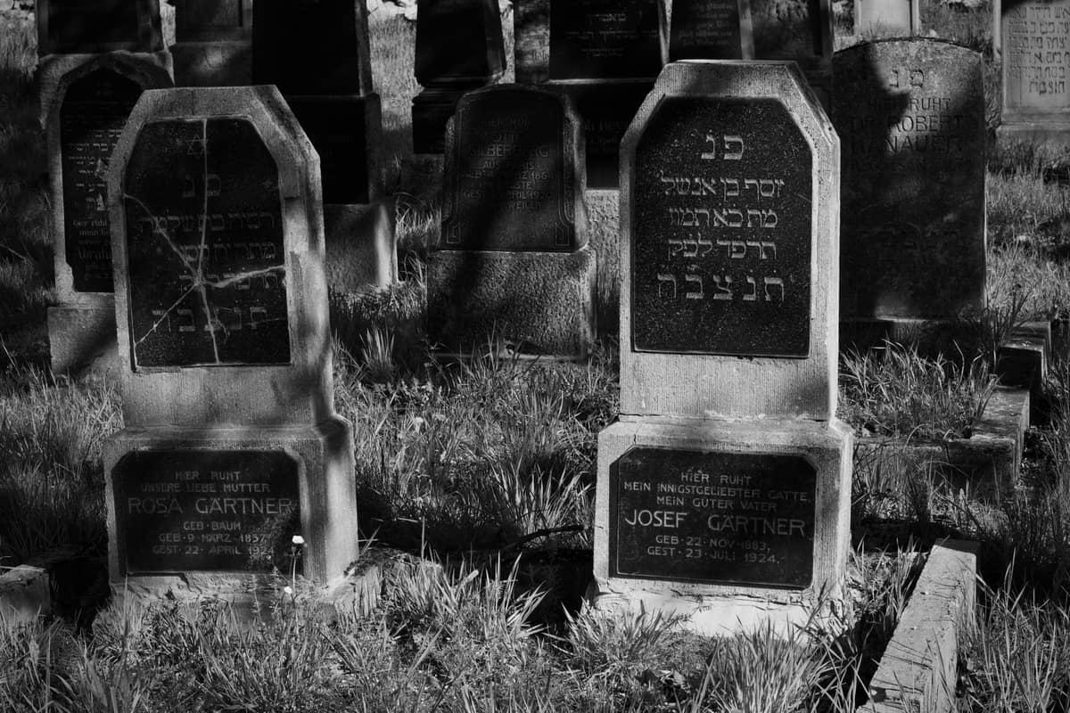 Foto en blanco y negro de antiguas lápidas judías con inscripciones en hebreo, cubiertas de hierba, en un cementerio histórico