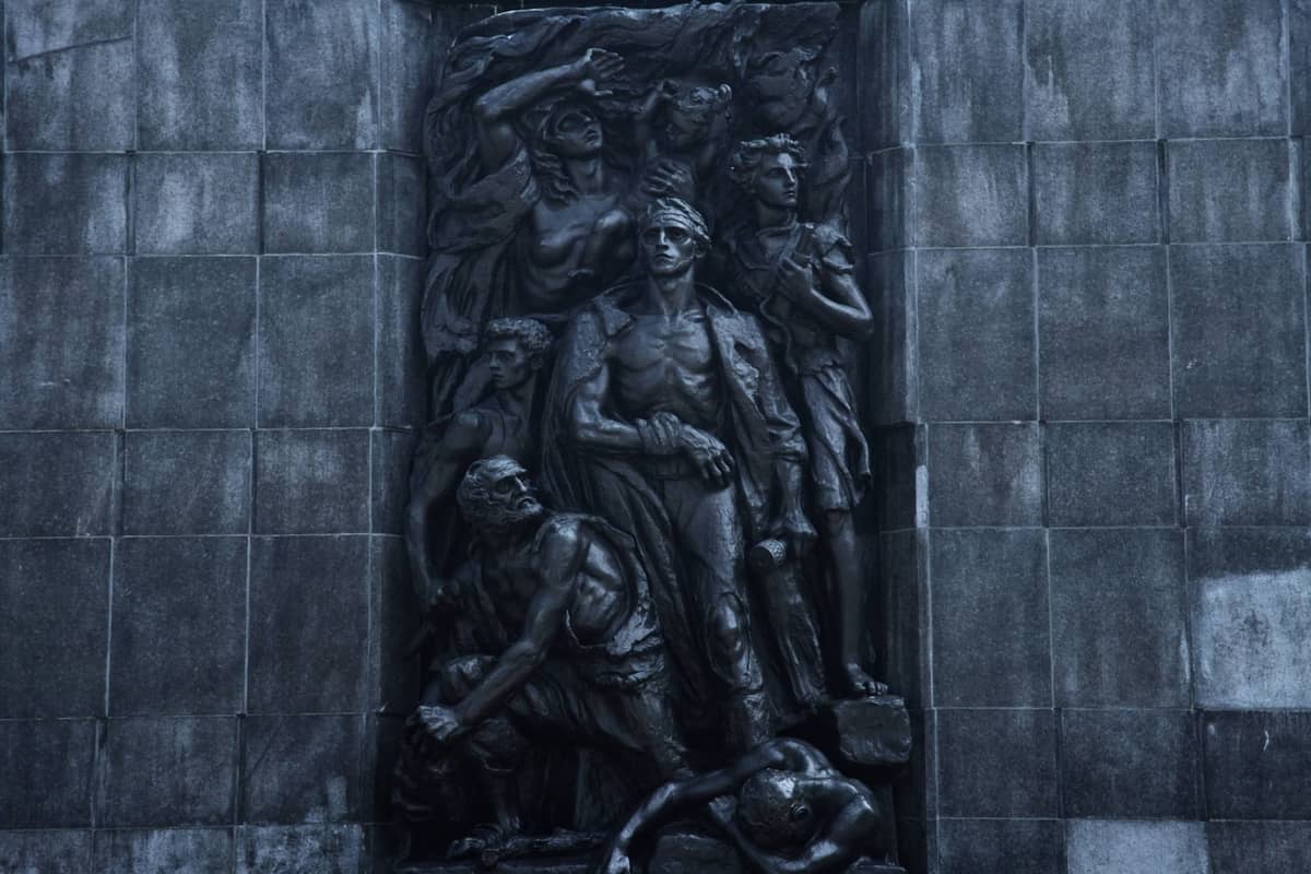 Primer plano de la escultura en relieve del Monumento a los Héroes del Gueto de Varsovia, con figuras heroicas en bronce sobre una pared de piedra.