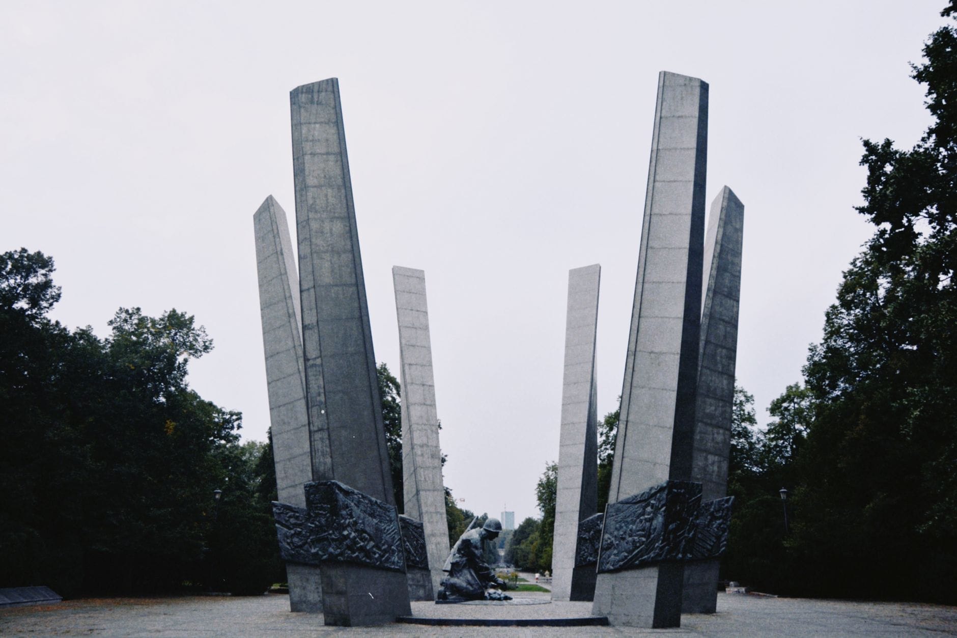 Vista ampla do Monumento aos Heróis do Gueto de Varsóvia, emoldurado por altos pilares de concreto e árvores — um dos principais marcos da história judaica na cidade.