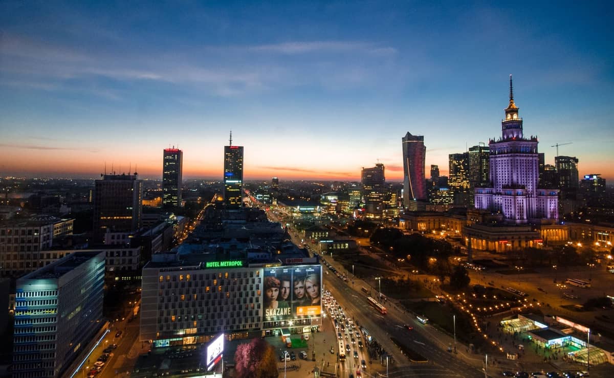 Vista elevata al tramonto del centro di Varsavia con moderni grattacieli e il illuminato Palazzo della Cultura e della Scienza che domina le strade trafficate.