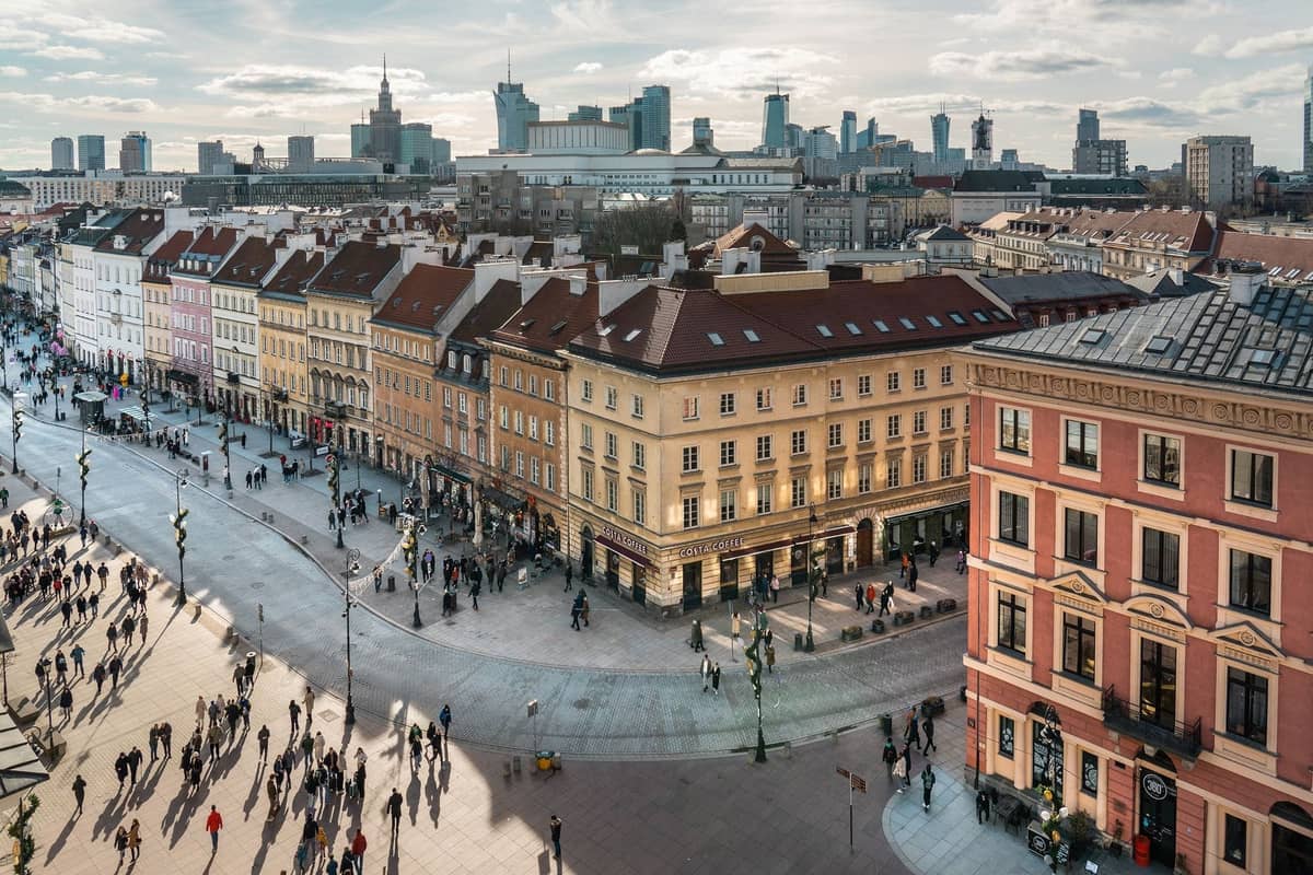 Una vivace strada di Varsavia con folle nel primo pomeriggio, edifici storici e lo skyline della città visibile sullo sfondo.