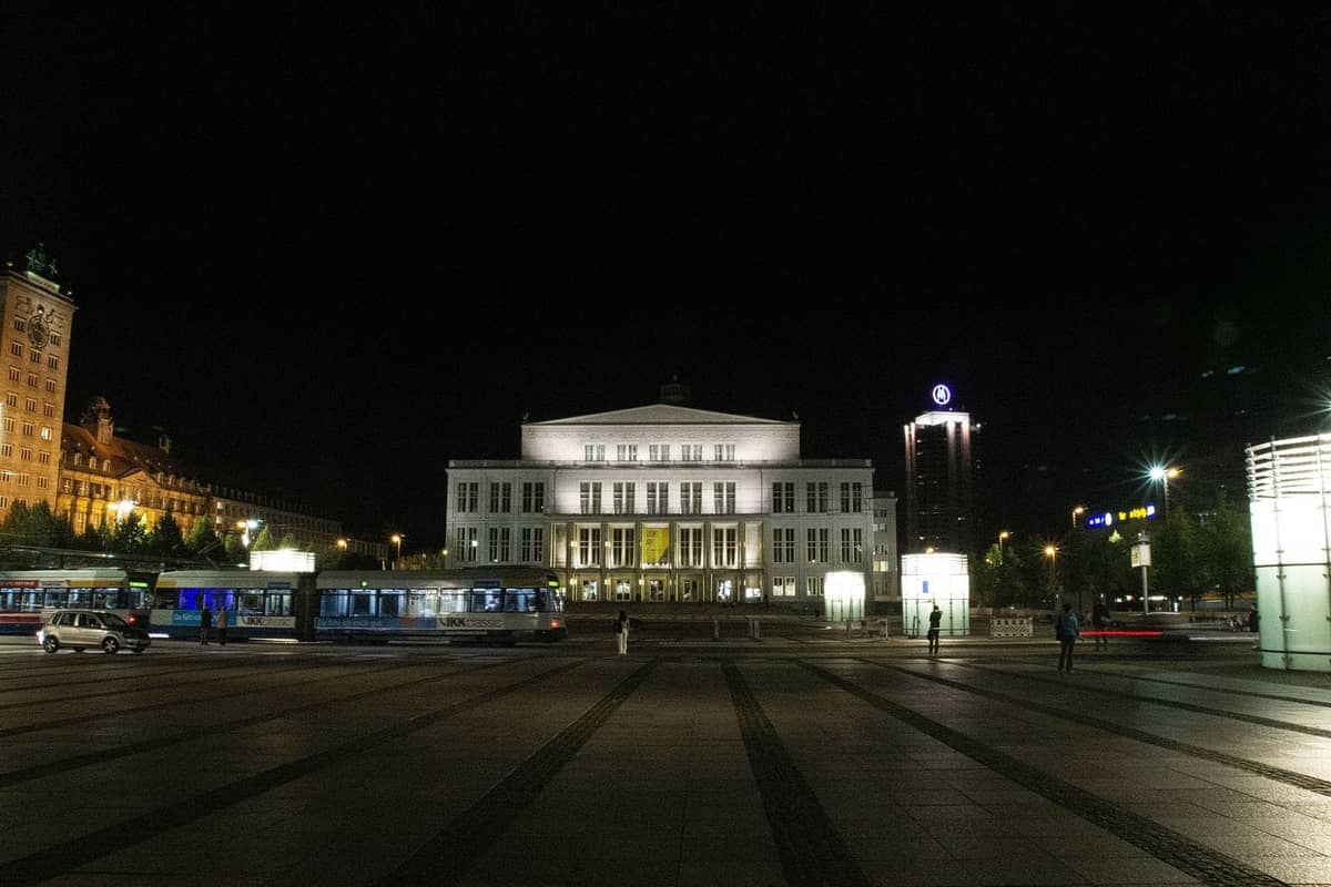 Vista notturna del Grand Theatre illuminato a Varsavia, con una piazza tranquilla e poche persone nei dintorni.