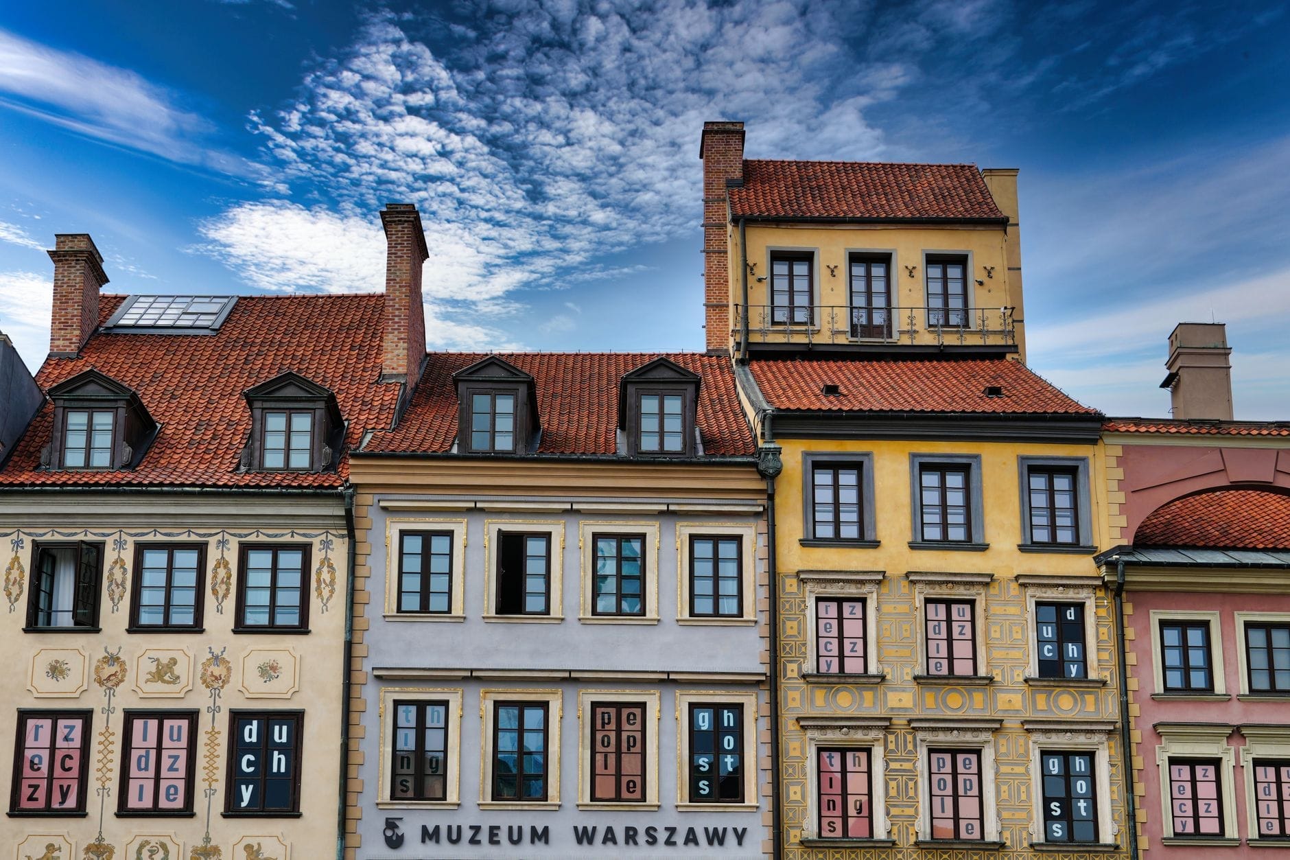 Prédios históricos coloridos com fachadas decoradas sob um céu azul vibrante na Cidade Velha de Varsóvia, com a placa do Museu de Varsóvia visível ao nível da rua.