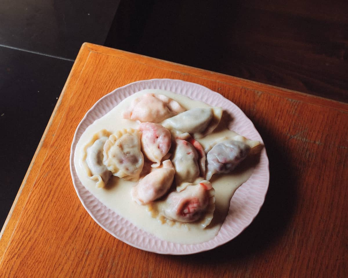 Ein Teller bunter polnischer Pierogi auf einem Holztisch, in natürlichem Licht gebadet