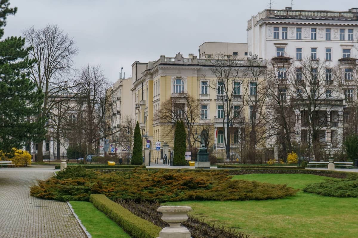 Parque urbano en Varsovia con setos bien recortados y majestuosos edificios circundantes, en un día nublado en el centro de la ciudad.