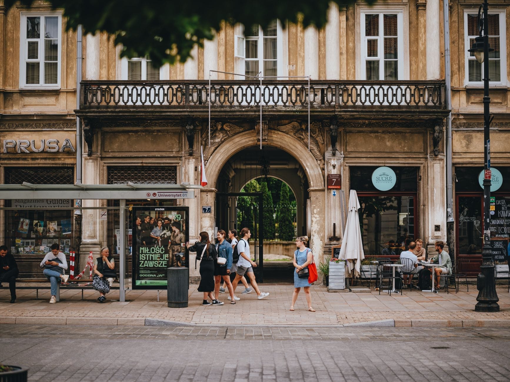 Rua animada de Varsóvia com pessoas caminhando entre lojas e cafés em frente a um prédio histórico, transmitindo uma atmosfera vibrante de compras.