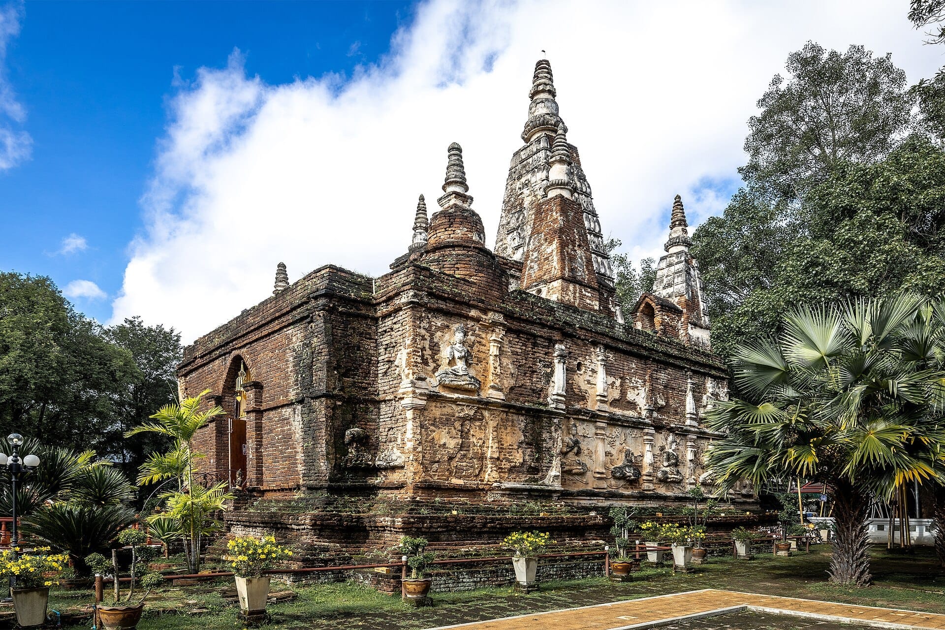 Công trình gạch cổ của Wat Jed Yod nổi bật với bảy tháp nhọn riêng biệt, những chạm khắc cũ kỹ và những cây xanh tươi tốt dưới bầu trời sáng rực.