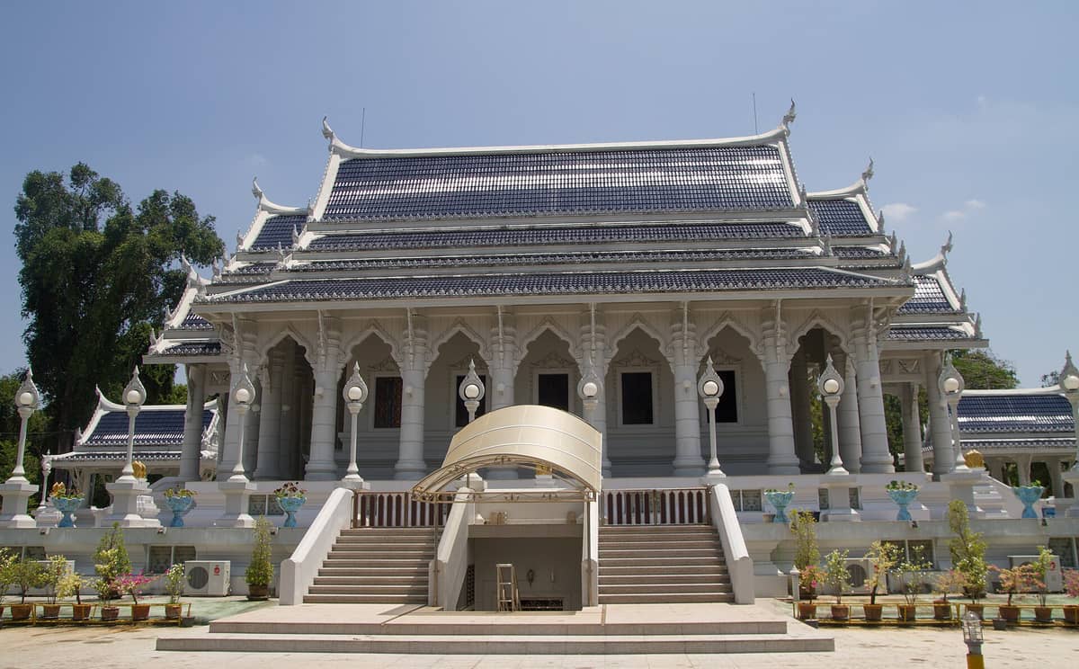 Frontansicht der prachtvollen weißen Haupthalle des Wat Kaew Korawaram in Krabi Town, mit einer Treppe davor und dekorativen blauen Dachziegeln unter klarem Himmel.