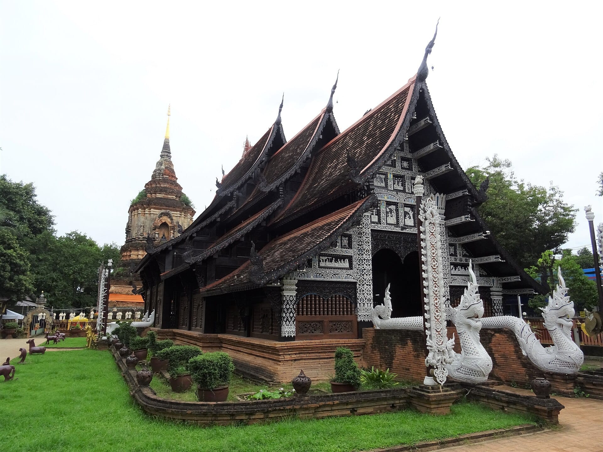 Chùa Wat Lok Moli ở Chiang Mai với kiến trúc gỗ tinh xảo, tượng rắn thần naga màu trắng ở lối vào và tháp chedi bằng gạch cổ ở phía sau.