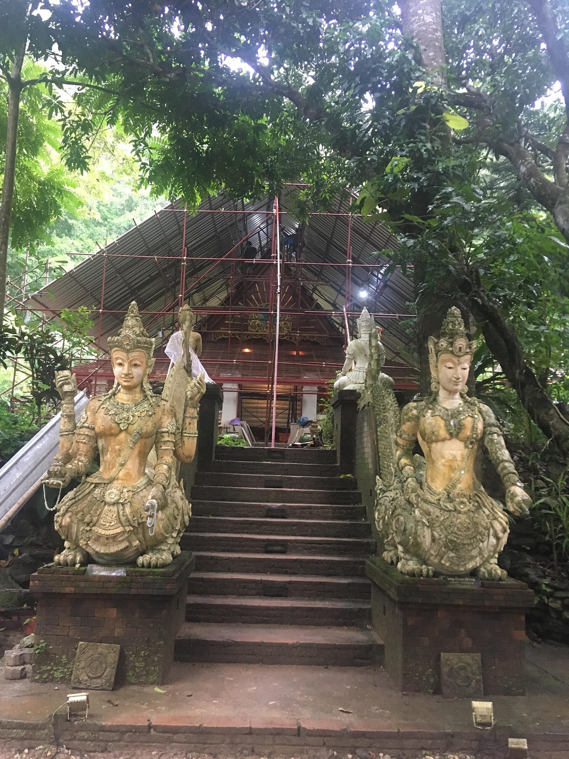 Estatuas de piedra custodian los peldaños cubiertos de musgo que conducen a un edificio del templo en Wat Pha Lat, enclavado entre densas y verdes selvas.