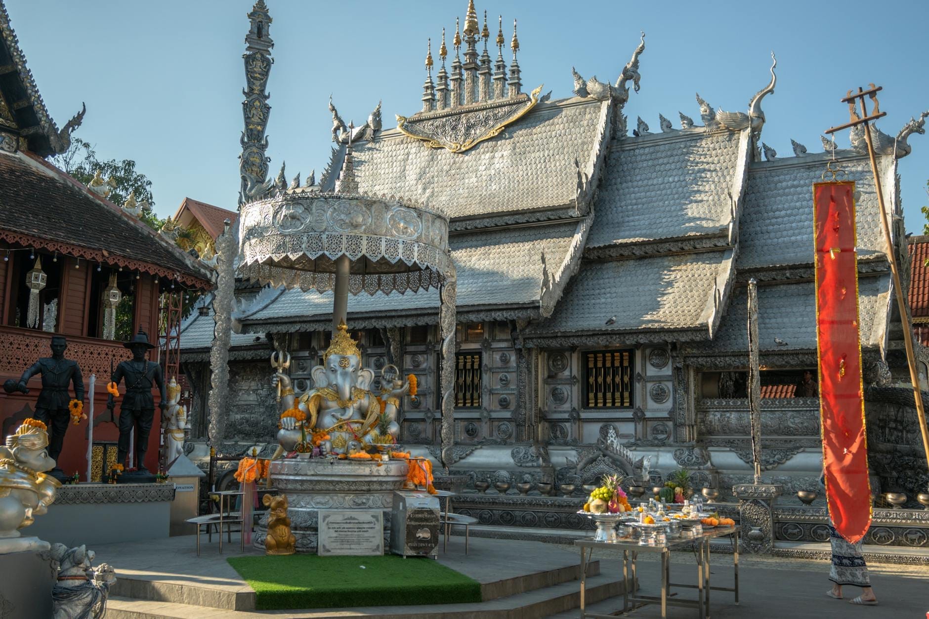 El exterior revestido de plata del Wat Sri Suphan en Chiang Mai, con elaborada ornamentación metálica y un santuario al frente bajo un cielo azul despejado.