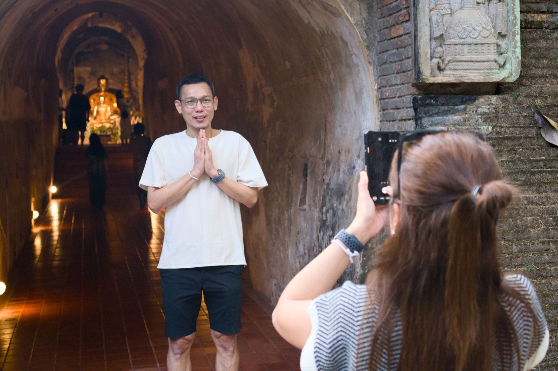 Hai người bên trong đường hầm gạch cổ của Wat Umong, một người đang chụp ảnh người kia đứng gần tượng Phật ở cuối hầm.