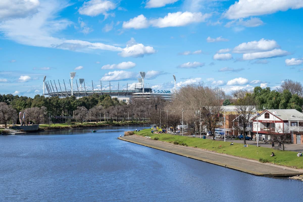 Widok przez rzekę Yarra w Melbourne w kierunku stadionu MCG w słoneczny dzień z błękitnym niebem i rozproszonymi chmurami.