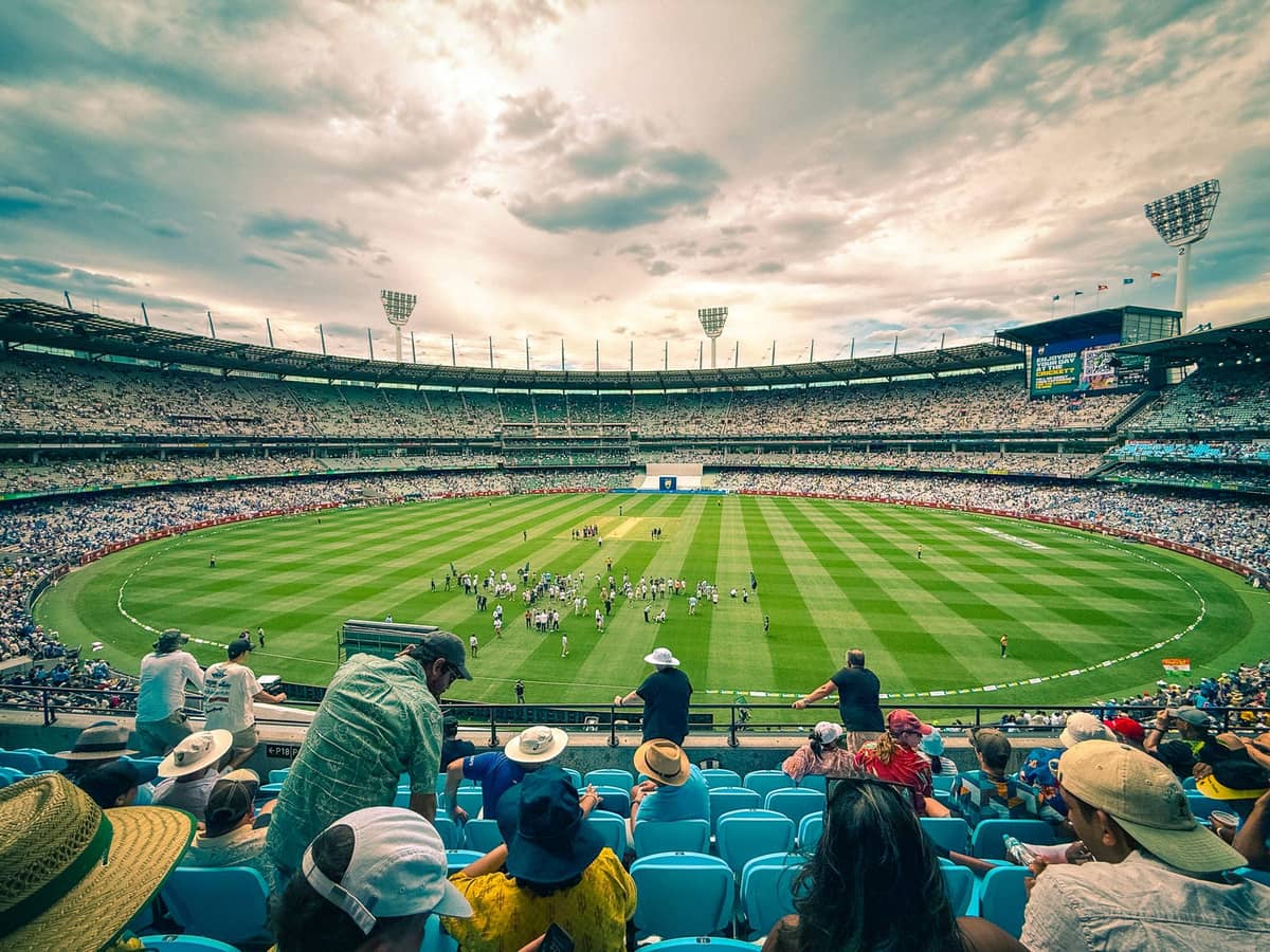 El Melbourne Cricket Ground (MCG) lleno de hinchas en las tribunas viendo un partido en vivo bajo un cielo nublado.