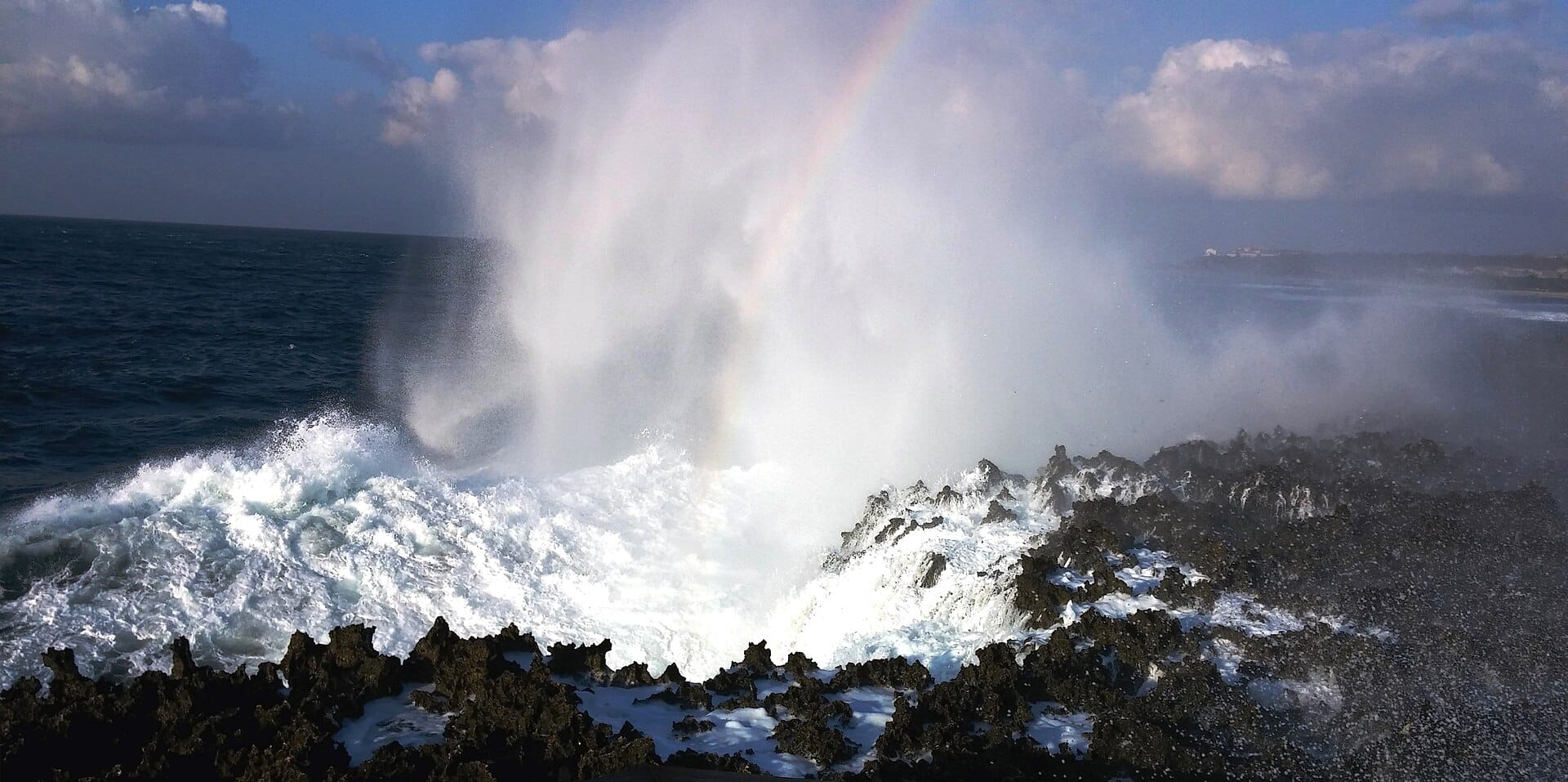 Onde potenti che eruttano attraverso rocce vulcaniche al Waterblow Nusa Dua, Bali, inviando getti d'acqua marina in alto nel cielo.