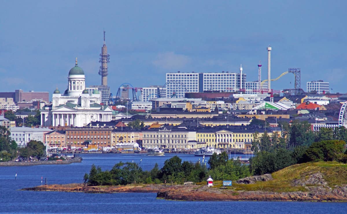 Vista ampla da orla de Helsinque com o skyline da cidade, a Catedral de Helsinque e as ilhas do arquipélago em primeiro plano sob um céu azul e limpo.