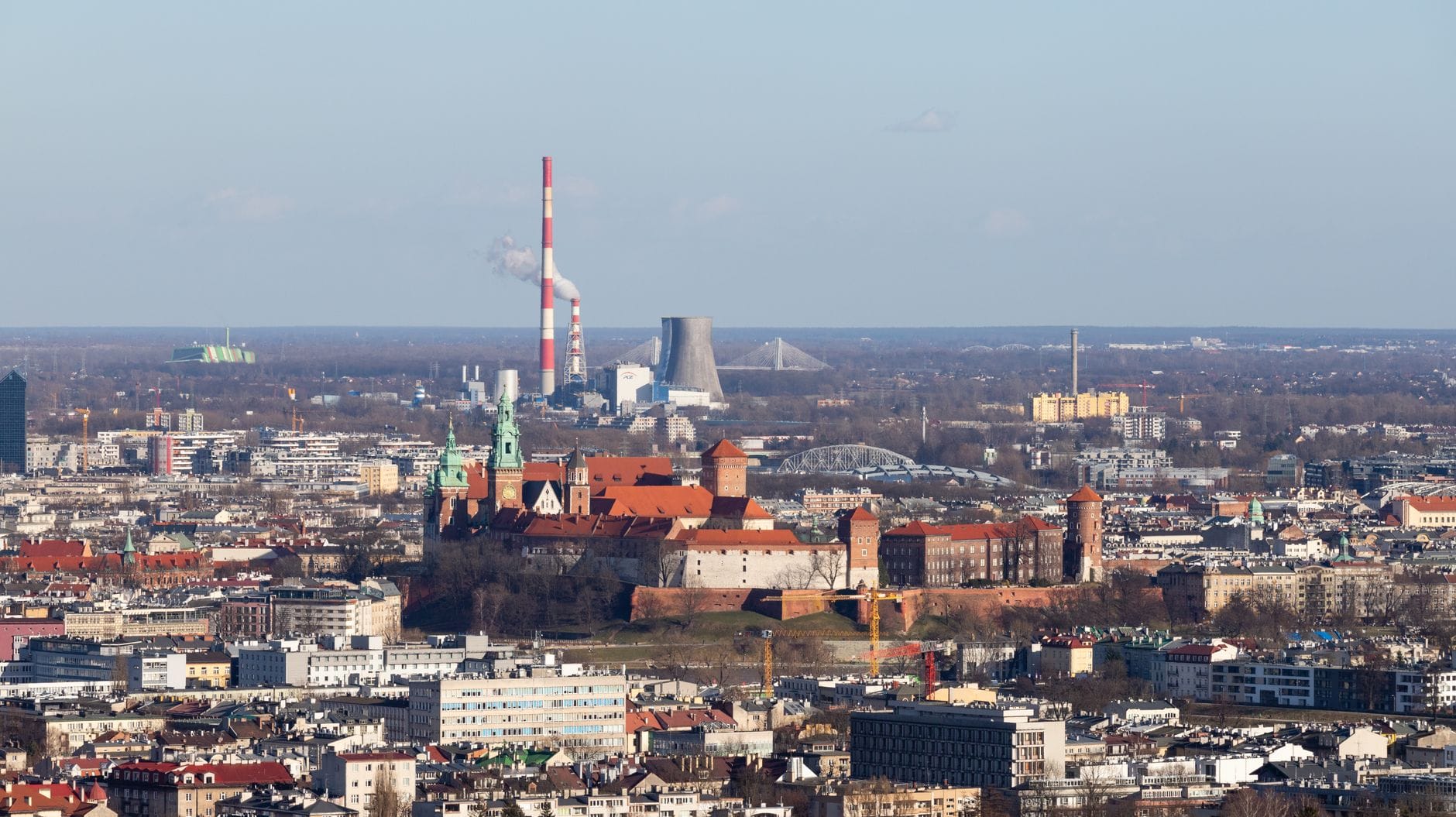 มุมมองทางอากาศของเนิน Wawel แสดงให้เห็นกลุ่มอาคารปราสาทที่ตั้งตระหง่านเหนือทิวทัศน์เมือง Kraków พร้อมหอคอยและหลังคาสีแดงที่มองเห็นได้อย่างชัดเจน