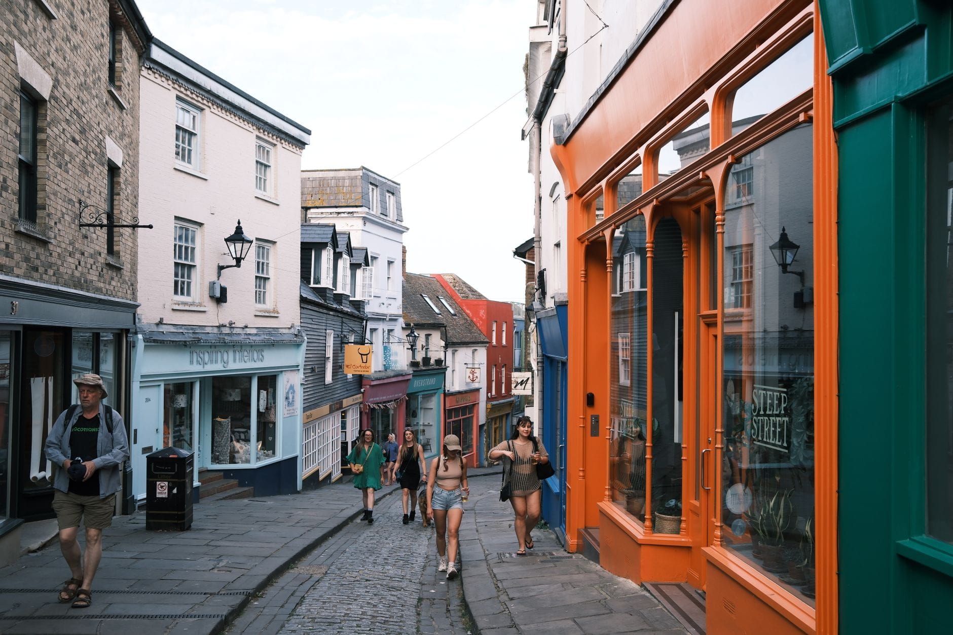 Persone che camminano lungo una strada stretta e colorata fiancheggiata da negozi indipendenti e caffè nel quartiere North Laine di Brighton.