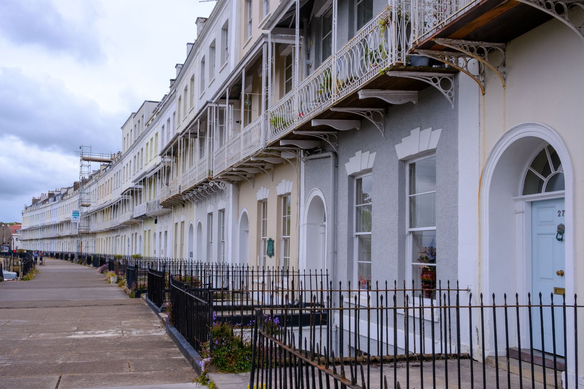 Fila di case a schiera in stile Regency dipinte in colori pastello con ringhiere in ferro lungo un ampio marciapiede, tipiche dell'architettura di Kemp Town a Brighton.