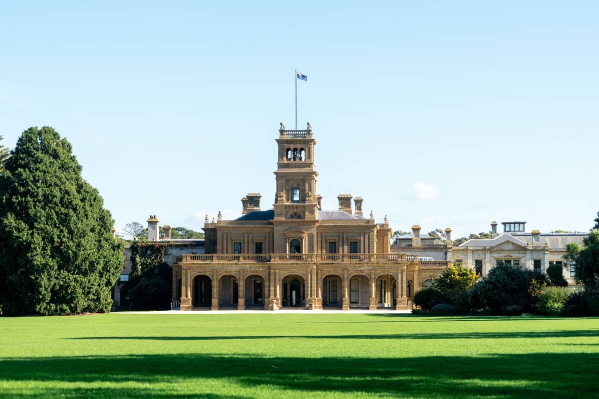 Werribee Park Mansion vom Rasen aus gesehen – Renaissance-Revival-Architektur mit imposantem Turm und üppigem Grün unter strahlend blauem Himmel.